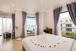 Habitación de hotel con una cama grande, vista al mar y balcón con mesa y sillas.