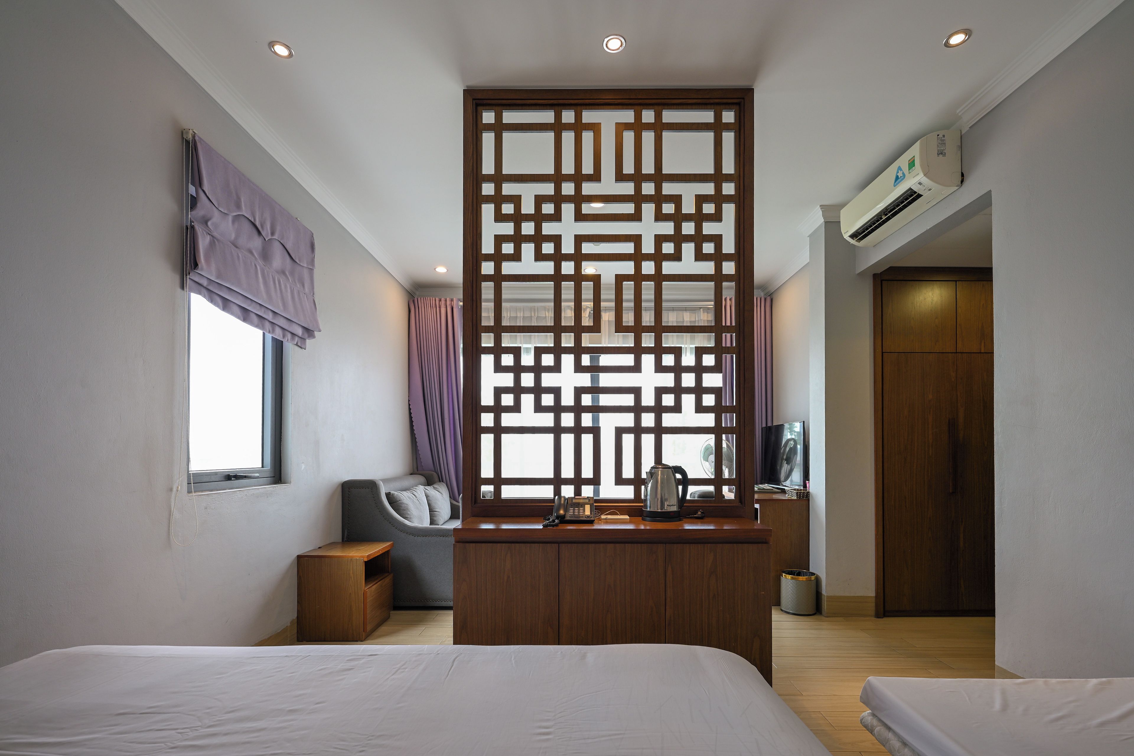 Une chambre d’hôtel comprenant un lit, un bureau avec une bouilloire, une chaise, une fenêtre avec des rideaux et un appareil de climatisation.
