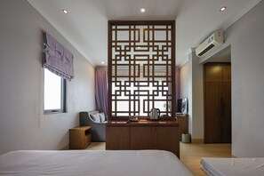 Habitació d'hotel amb un llit, una escriptori amb una paperera, una cadira, una finestra amb cortines i un aparell d'aire condicionat.