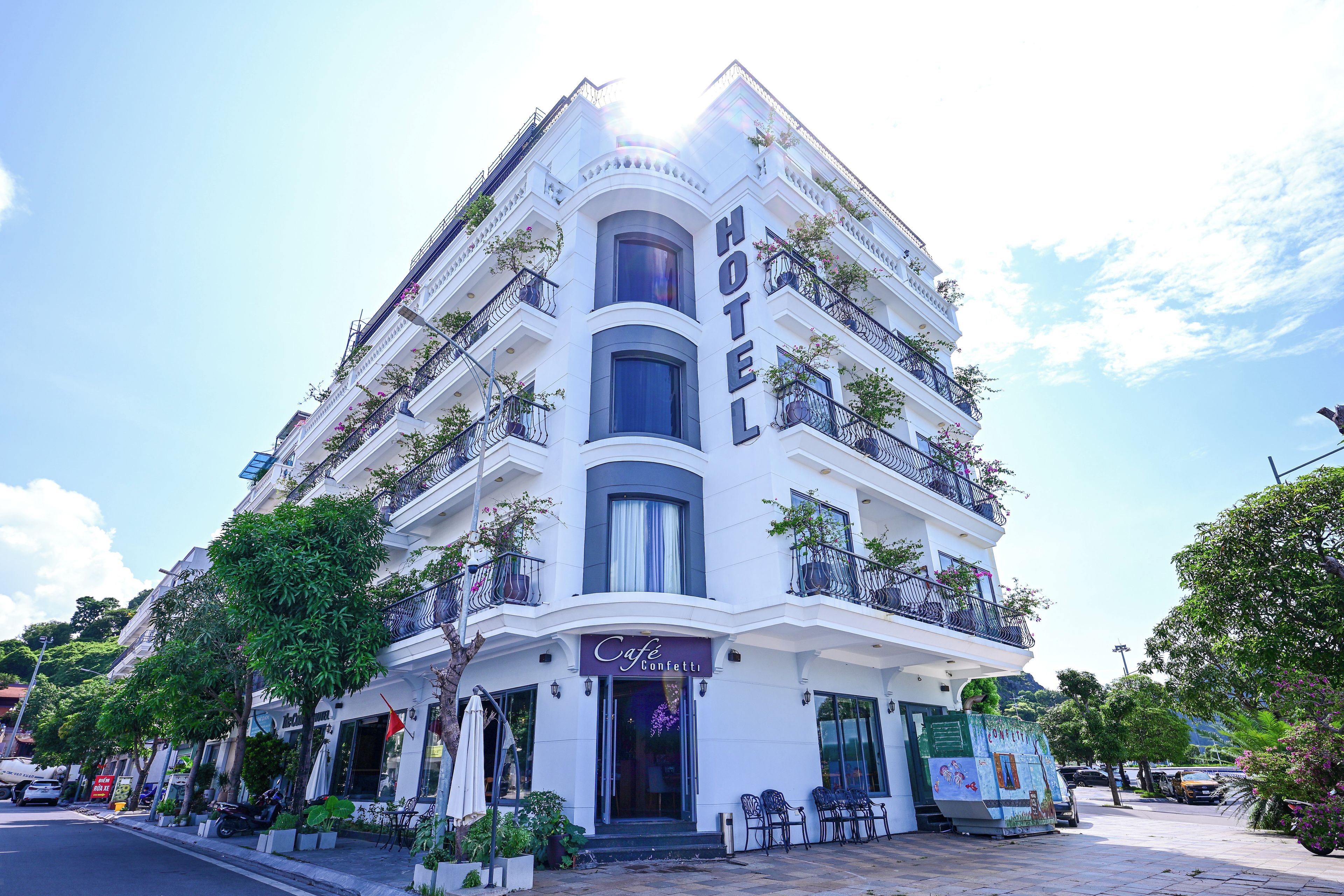 Un hotel de varios pisos con balcones, un café y mesas al aire libre.