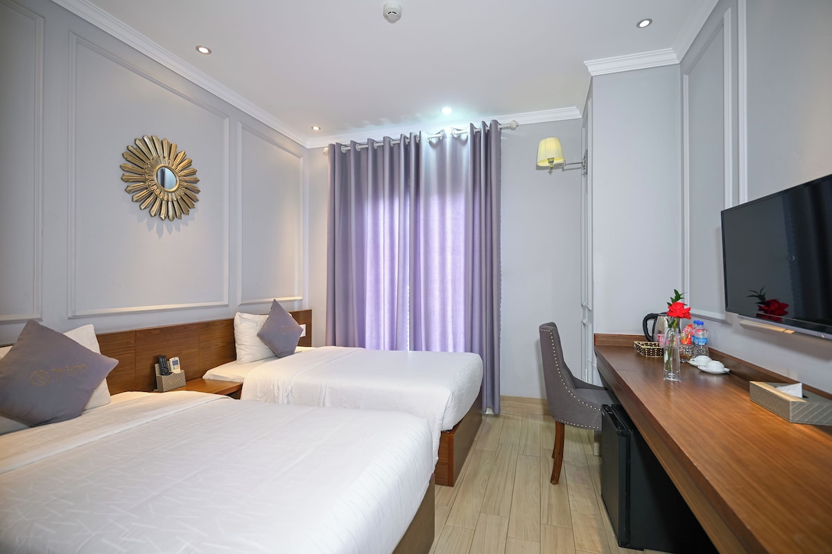 Habitación de hotel con dos camas, un escritorio, televisor, espejo y ventana con cortinas.