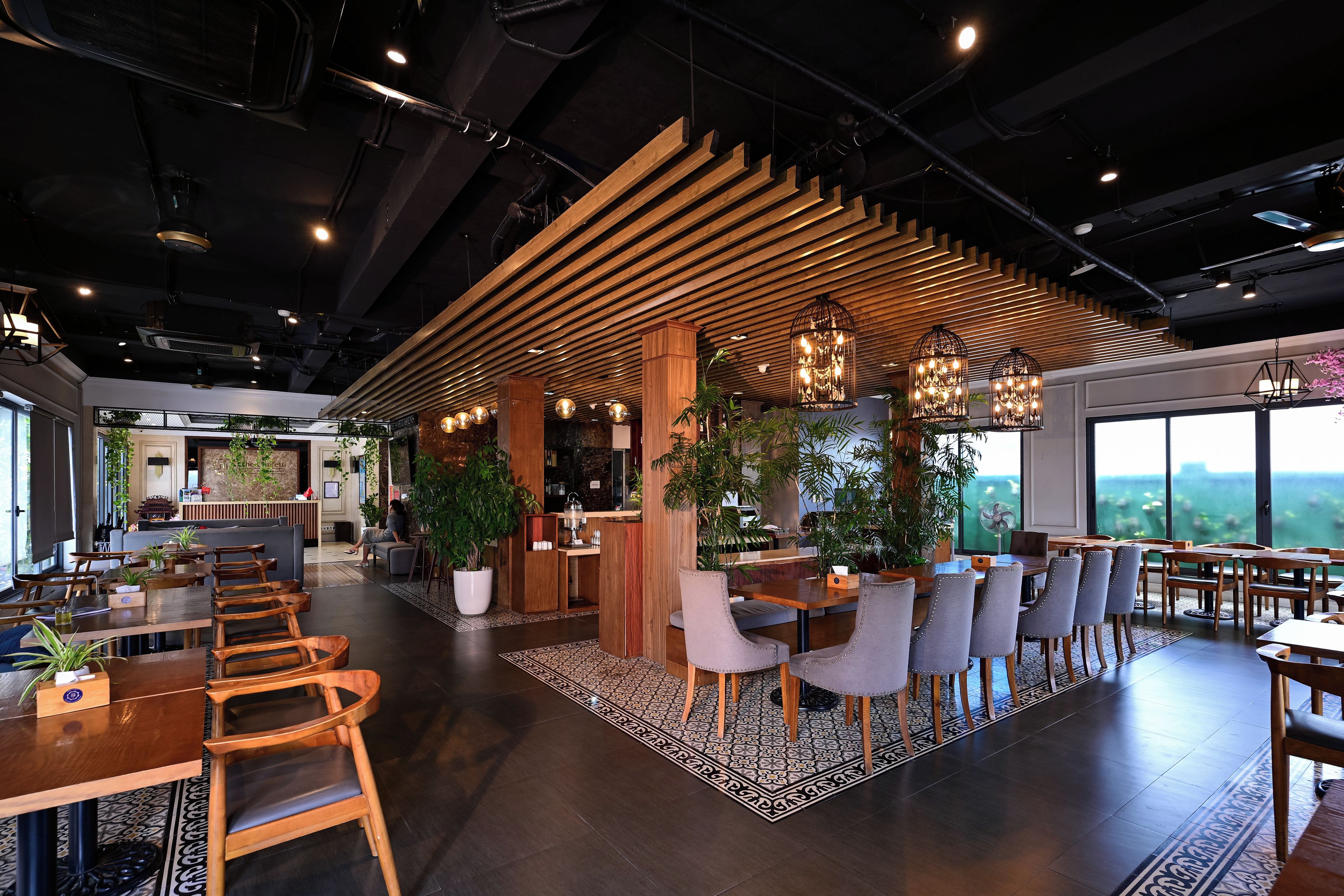 A modern interior with wooden ceiling slats, a reception desk, and seating areas with tables and chairs.