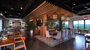 A modern interior with wooden ceiling slats, a reception desk, and seating areas with tables and chairs. - The Confetti Hotel Ha Long (Hong Gai)