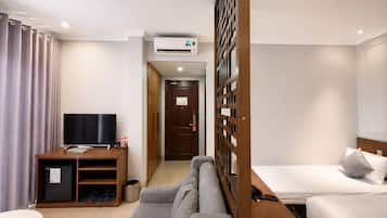 A hotel room with a TV, sofa, bed, and a wooden partition.