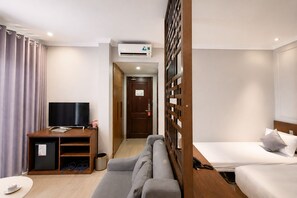 A hotel room with a TV, sofa, bed, and a wooden partition. - The Confetti Hotel Ha Long (Hong Gai)