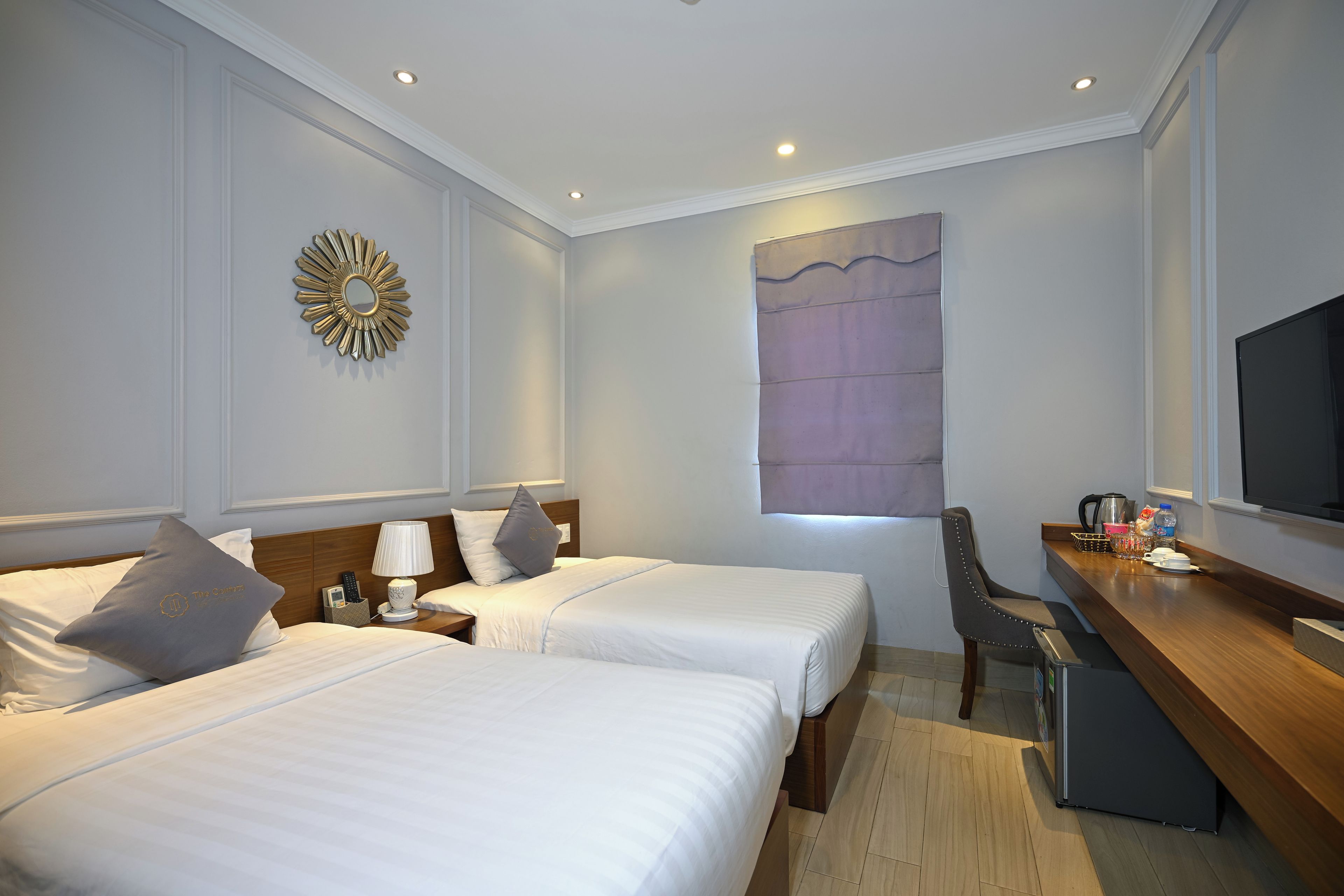 A hotel room with two beds, a desk with a chair, a television, and a large window.