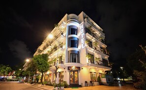 Un hotel de varios pisos con un letrero grande que dice 'HOTEL', un área de estar al aire libre y balcones con plantas.