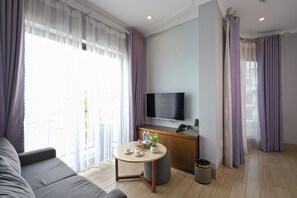 A modern living room with a sofa, a round coffee table, a TV, and a small kitchenette area. - The Confetti Hotel Ha Long (Hong Gai)