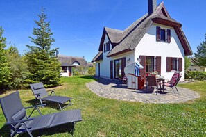 A house with a thatched roof, a patio with outdoor furniture, and a well-maintained lawn. - Vacation home with a fireplace and sauna, about 300 meters from the sandy beach; pets welcome (Glowe)