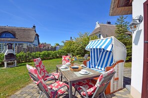 An outdoor dining area with a wooden table and chairs, a barbecue grill, and a striped awning. - Vacation home with a fireplace and sauna, about 300 meters from the sandy beach; pets welcome (Glowe)