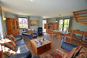 A spacious living room with a fireplace, leather sofas, a wooden dining table, and a large window providing natural light. - Vacation home with a fireplace and sauna, about 300 meters from the sandy beach; pets welcome (Glowe)