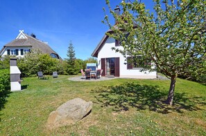 A house with a thatched roof, a garden with a table and chairs, and a large rock in the foreground. - Vacation home with a fireplace and sauna, about 300 meters from the sandy beach; pets welcome (Glowe)