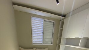 Quarto com cama, janela com persianas e estantes embutidas.