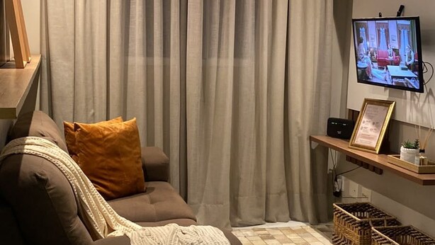 Sala de estar com sofá, televisão e prateleira fixada na parede.