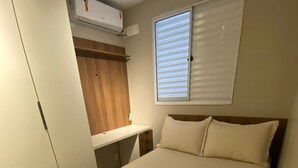 Quarto com cama, escrivaninha, guarda-roupa e janela com persianas.