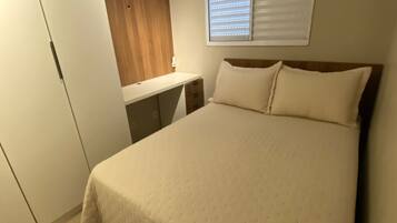 Un dormitorio con cama, escritorio, armario y ventana con persianas.