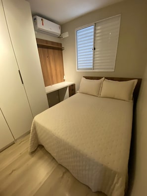 Un dormitorio con cama, escritorio, armario y ventana con persianas.