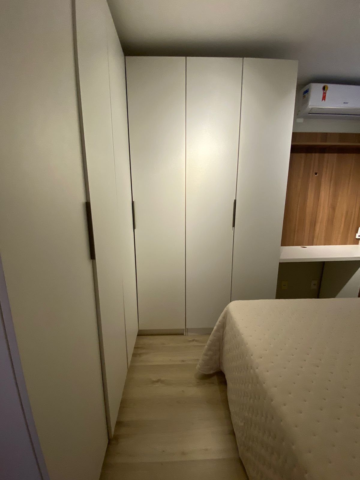 Un pasillo estrecho con una cama al final, un armario y una pequeña zona de cocina.