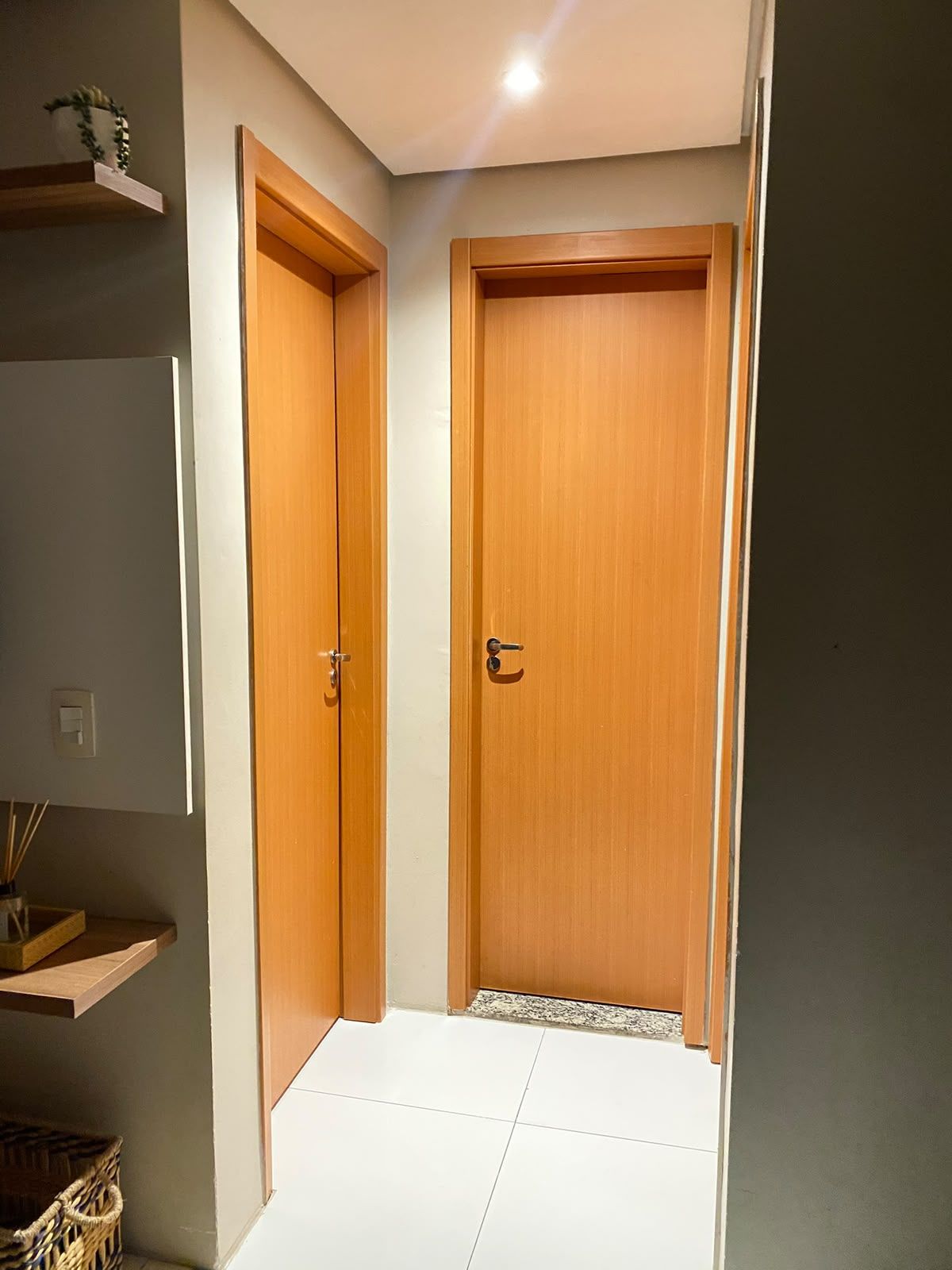 Un pasillo con dos puertas de madera, un estante pequeño con una planta y una cesta en el suelo.