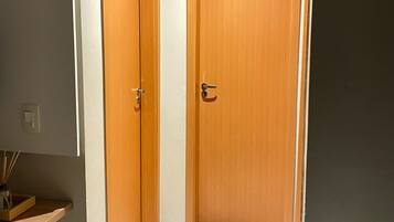 Un pasillo con dos puertas de madera, un estante pequeño con una planta y una cesta en el suelo.