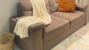 Uma sala de estar moderna com um sofá marrom, um cobertor branco e uma almofada laranja. Há duas obras de arte emolduradas na parede acima do sofá.