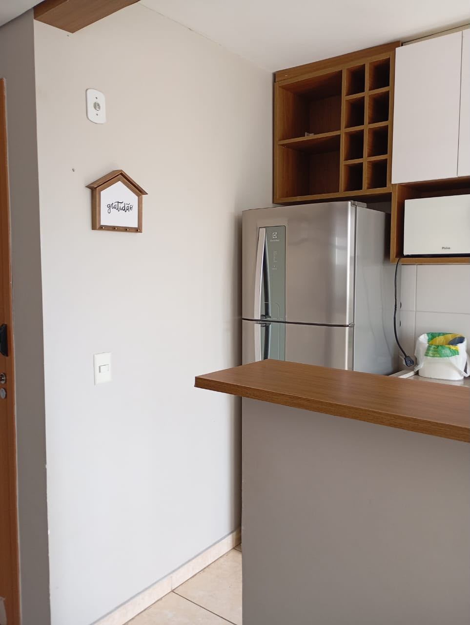 Una cocina con un refrigerador de acero inoxidable, armarios de madera y una pequeña estantería.