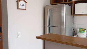 Una cocina con un refrigerador de acero inoxidable, armarios de madera y una pequeña estantería.