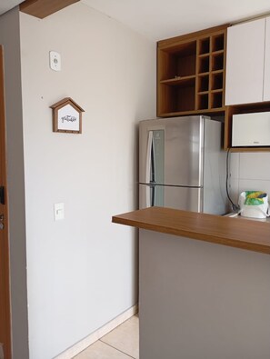 A kitchen with a stainless steel refrigerator, wooden cabinets, and a small shelf.