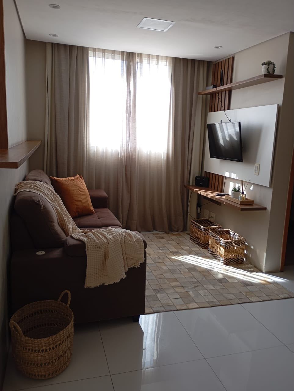 Una sala de estar con sofá, televisión y un ventanal con cortinas.