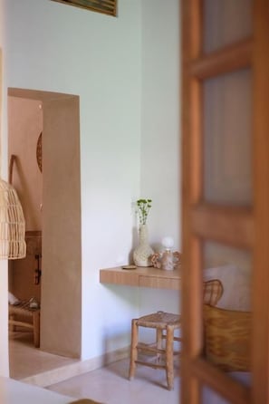 A room with a wooden door, a wicker chair, a small stool, and a shelf with decorative items. - Riad L'Atelier (Marrakech)