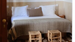 A bedroom with a bed, two wooden stools, a woven ceiling light, and a wall-mounted decorative item. - Riad L'Atelier (Marrakech)