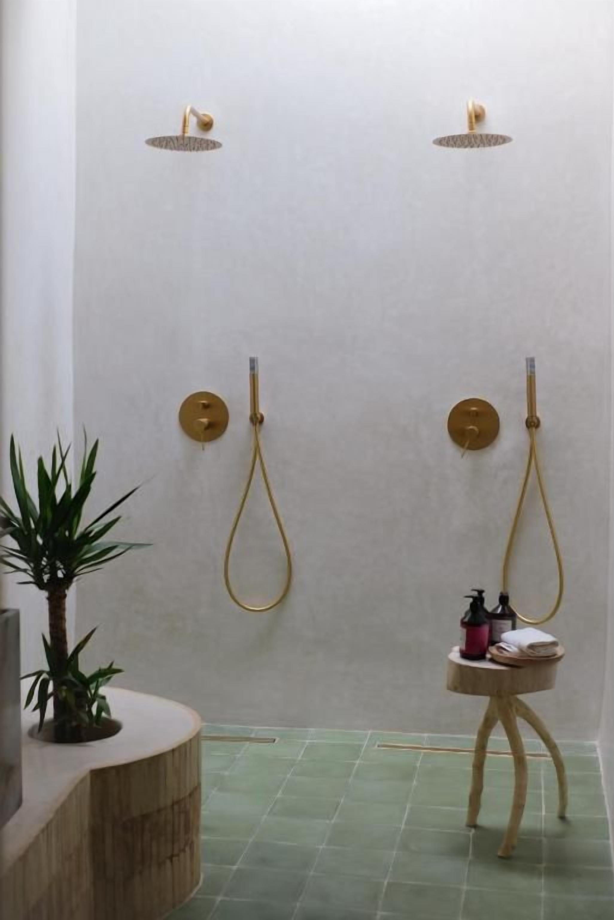 A bathroom with two showerheads, a small wooden stool with toiletries, and a potted plant.