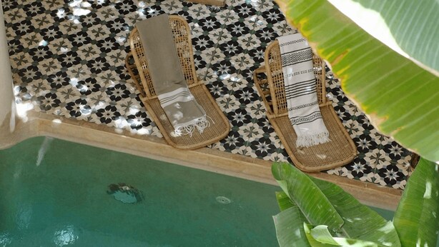 A pool area with two wicker lounge chairs and a tiled floor. - Riad L'Atelier (Marrakech)