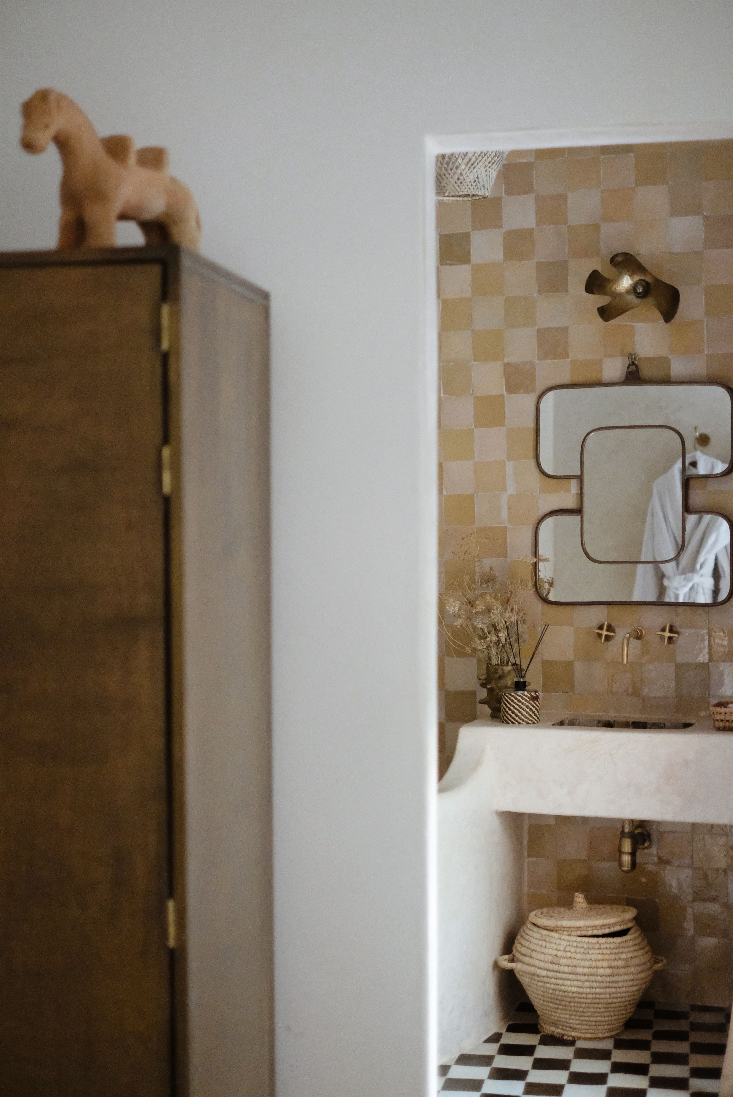 Um banheiro com painel de azulejos xadrez, espelho, armário de madeira e pia com porta-toalhas.