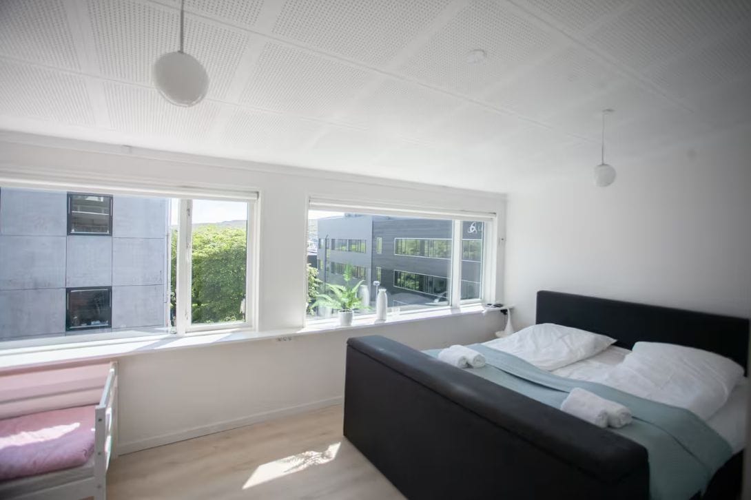 A modern bedroom with a bed, a bench, and large windows.