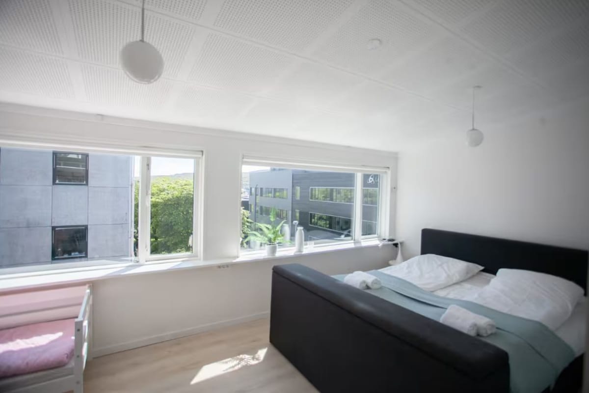 A modern bedroom with a bed, a bench, and large windows.
