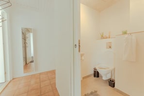 A bathroom with a toilet, bidet, and a small shelf with toiletries. - Bøkjarabrekka (Tórshavn)