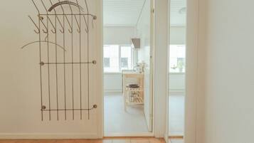 Una habitación con un tendedero metálico apoyado en una pared, una puerta de madera que da a otra habitación y un suelo de baldosas.