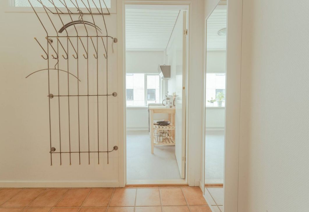 A room with a metal drying rack against a wall, a wooden door leading to another room, and a tiled floor.