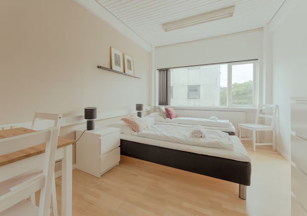 A modern bedroom with a bed, bedside tables, a desk, and a window.