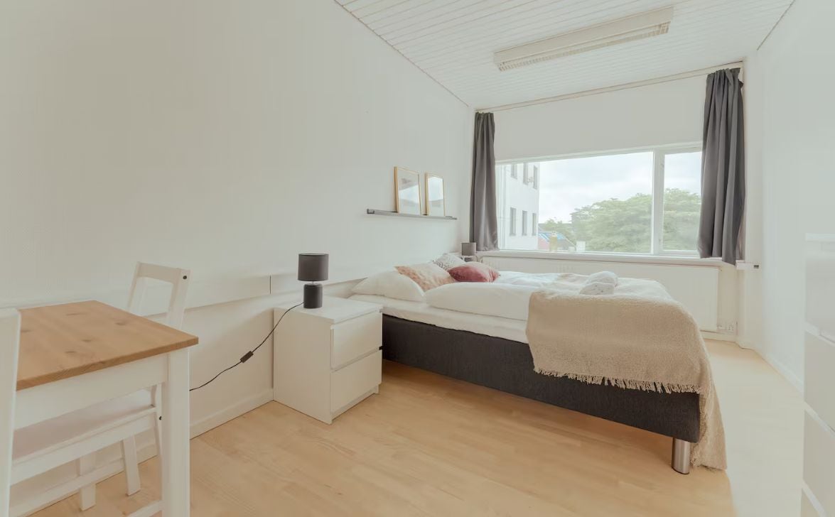 A minimalist bedroom with a bed, bedside table, and a window with curtains.
