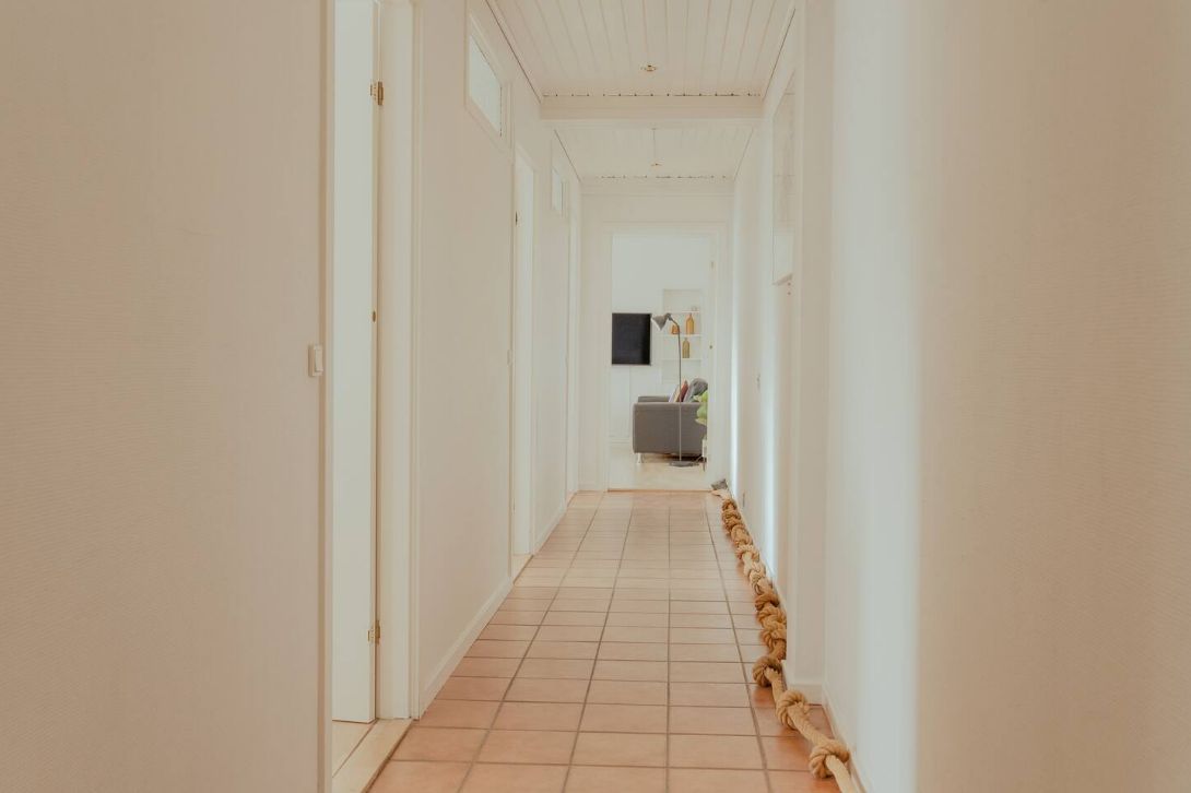 A hallway with a tiled floor, white walls, and a door on the left.