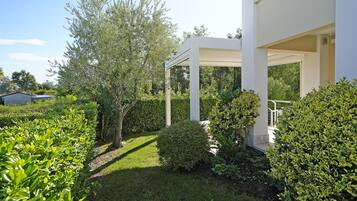 A well-maintained garden with a white pergola structure, surrounded by various shrubs and trees.