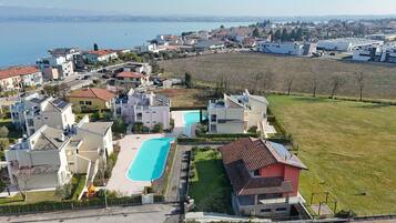 A residential area with a large swimming pool, houses with solar panels, and a view of the sea.