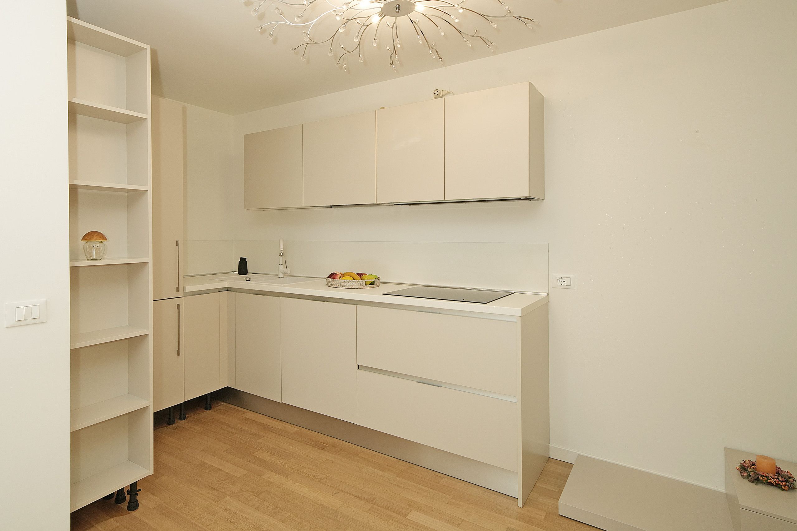 A compact kitchen with white cabinetry, a wooden floor, and a ceiling light fixture.