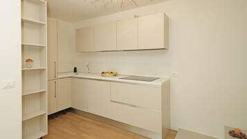 A compact kitchen with white cabinetry, a wooden floor, and a ceiling light fixture.
