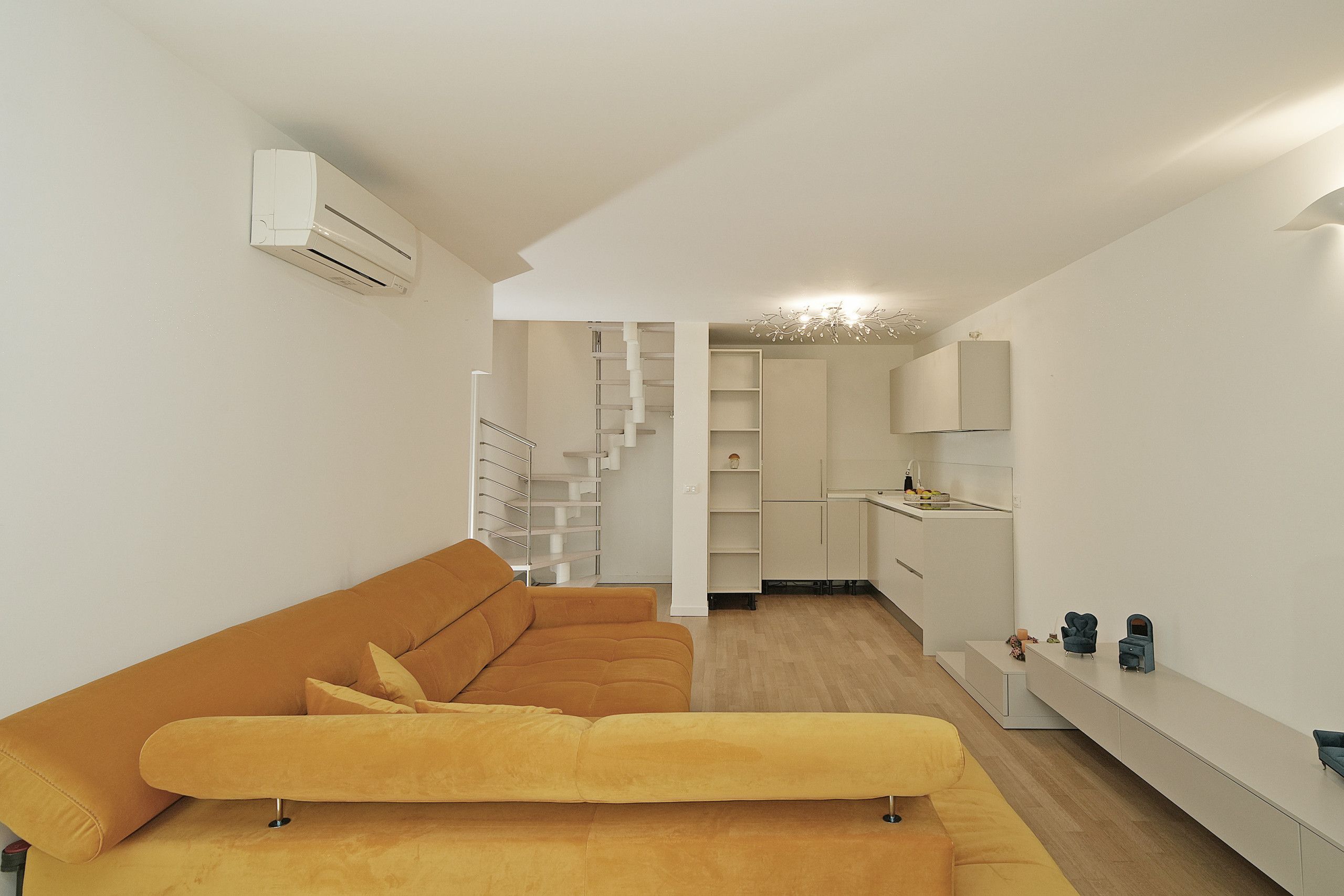 A modern living space with a sofa, a staircase, a kitchen area, and a built-in shelf.
