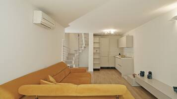 A modern living space with a sofa, a staircase, a kitchen area, and a built-in shelf.