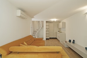 A modern living space with a sofa, a staircase, a kitchen area, and a built-in shelf. - Villetta I Giardini del Garda (Peschiera del Garda)
