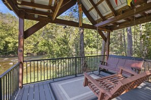 Eine Holzterrasse mit einer Bank, die auf einen Fluss mit Bäumen blickt.